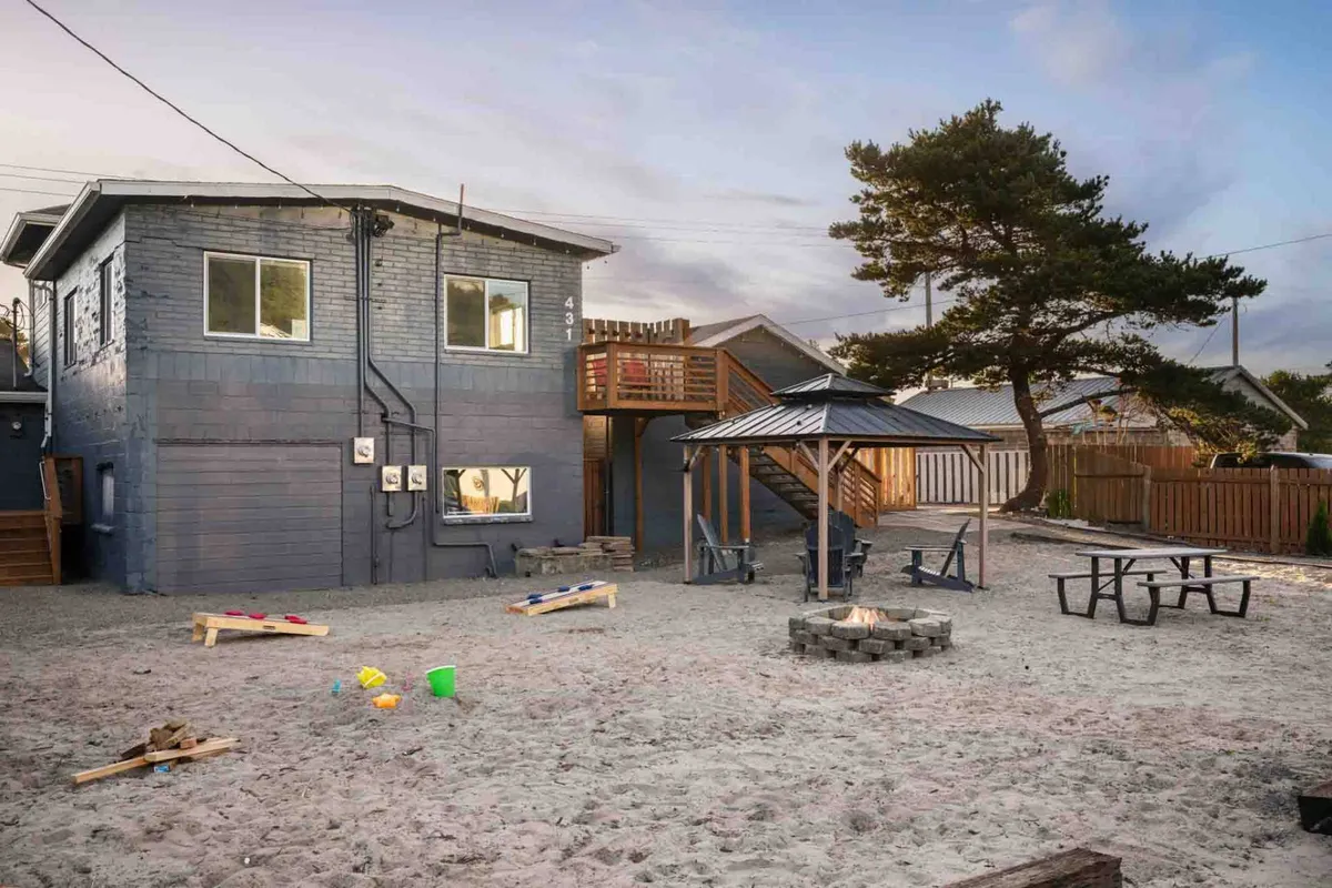 The exterior of a cozy cottage featuring a fire pit, picnic table, play area, and open spaces—an inviting scene for families and their pets to relax and spend time together outdoors.