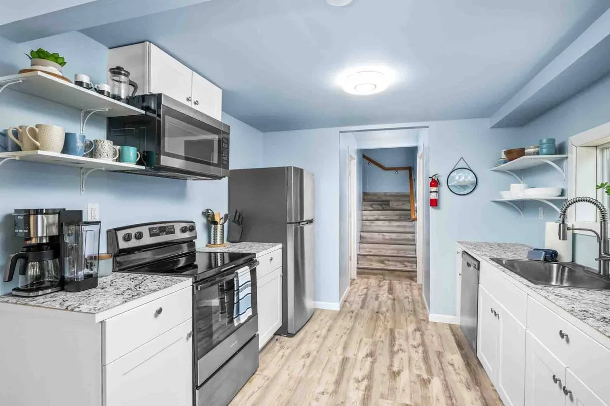 A welcoming kitchen scene featuring modern appliances, sleek countertops, and a visible staircase in the background. The space is bright and open, making it ideal for cooking and entertaining. The layout suggests plenty of room for multiple people to pitch in and prepare meals together.