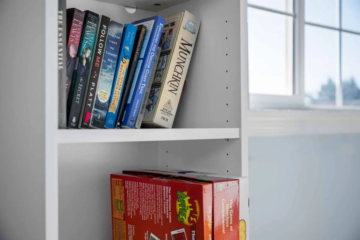 A cozy living area with a bookshelf filled with books, a game box, and inviting seating. The playful decor and accessible entertainment options evoke a family-friendly, relaxed atmosphere perfect for unwinding or enjoying spirited conversation and games.