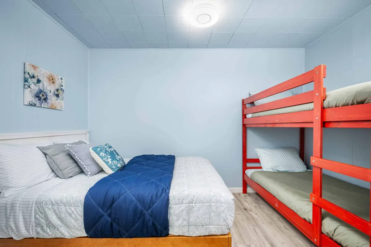A family-friendly bedroom showcasing a queen bed and a twin bunk bed, complemented by playful wall art. The layout invites both comfort and togetherness, making it ideal for children or friends traveling together.