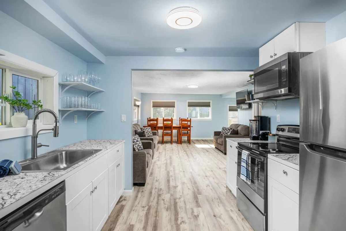 A cheerful interior showing the kitchen sink, granite countertops, a nearby dining area, and a comfortable sofa. The setting is open and modern, with updated features and a welcoming ambiance ideal for socializing or entertaining guests.