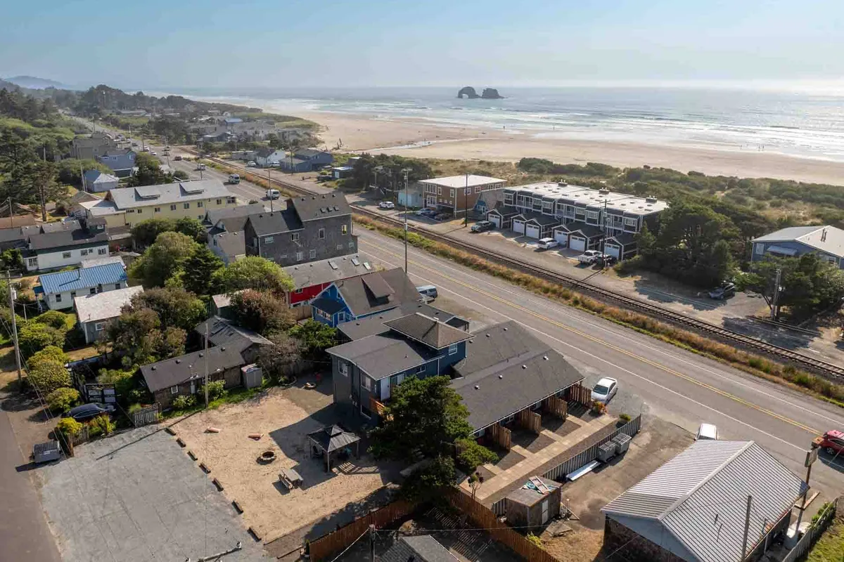 A wide, scenic view of the beach and ocean with distant rock formations, a road, and residential buildings. The image exudes an inviting, laid-back mood, showcasing the neighborhood's setting and the natural beauty of the nearby coastline.