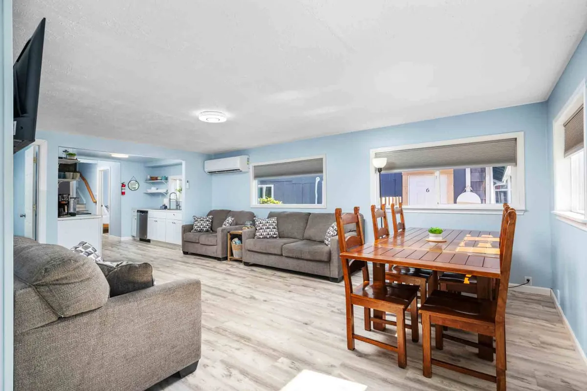 The image showcases a bright and welcoming open-concept living and dining area, featuring a large dining table perfect for shared meals, cozy sofas arranged for conversation or relaxation, and sun-filled windows that create a warm, inviting atmosphere.
