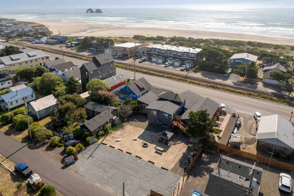 This exterior image captures the beach in the immediate foreground, with nearby houses, landscaped spaces, a road, and a visible play area. The sandy beach and outdoor play area evoke a sense of accessible coastal adventure and family fun.